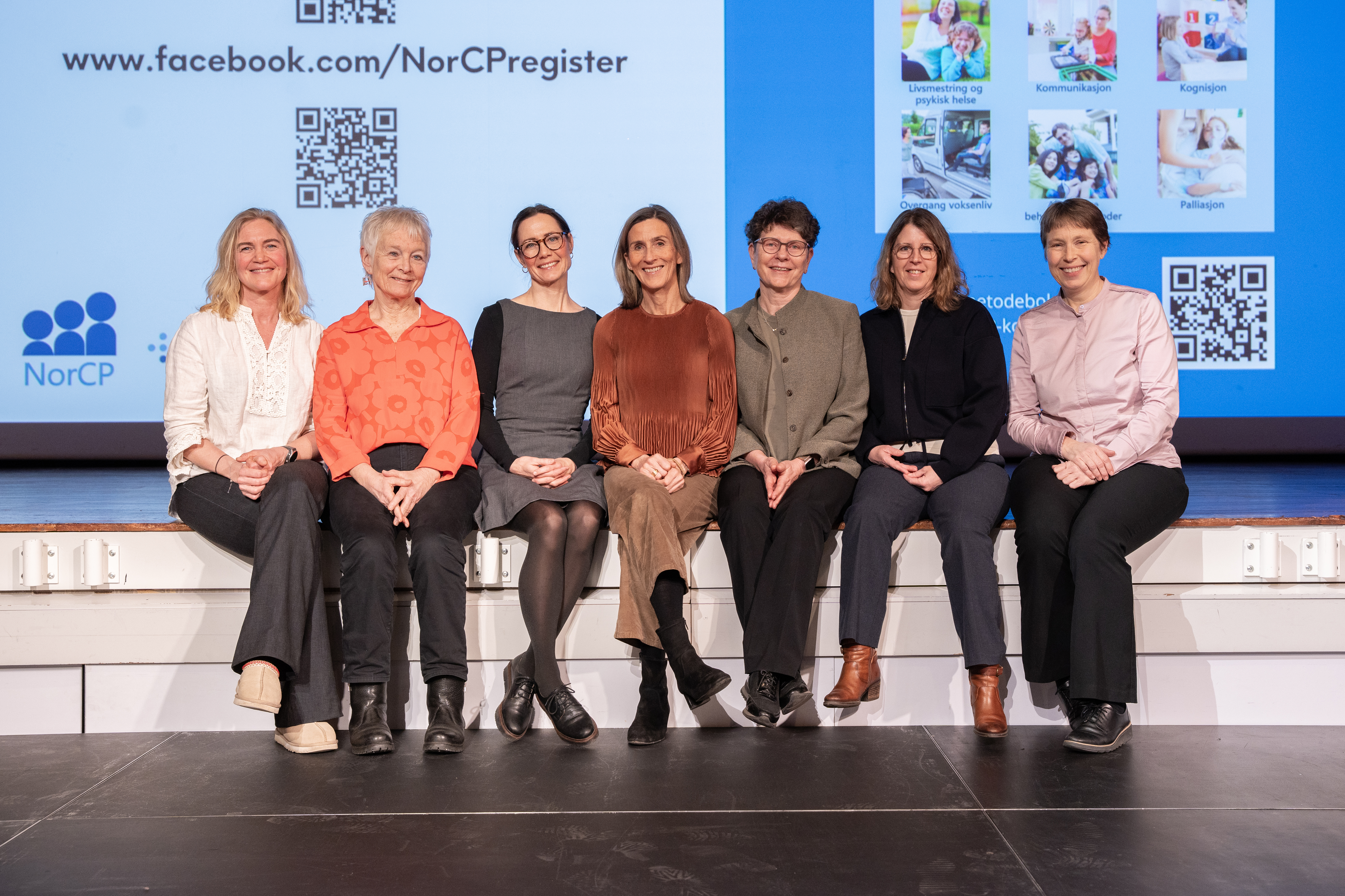 Sju kvinner som sitter på kanten av en scene