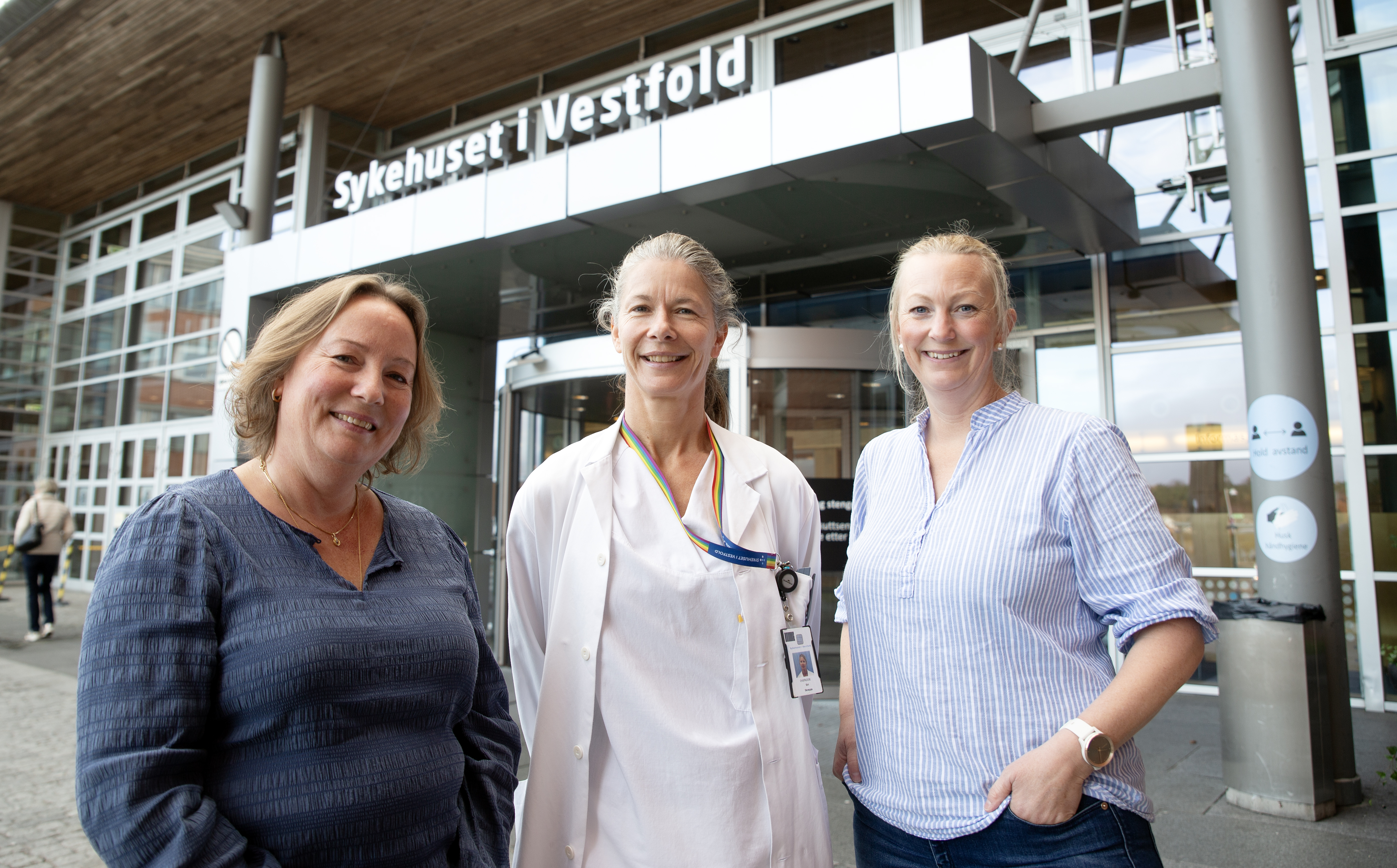 Tre smilende kvinner foran inngangsparti i glass og metall