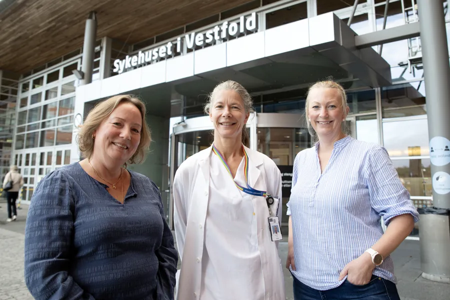 Tre smilende kvinner foran inngangsparti i glass og metall