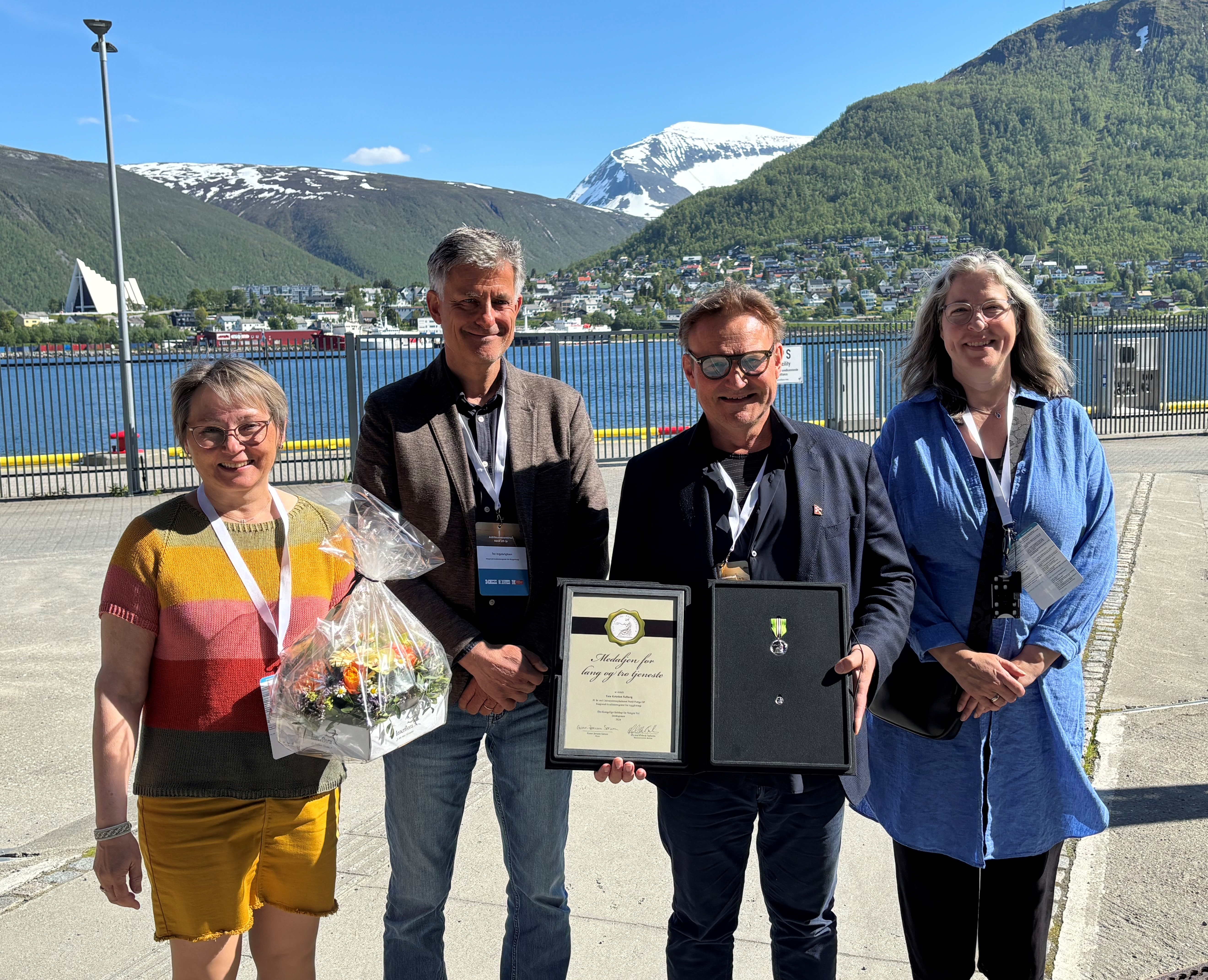 Fire personer som står ute med fjell i bakgrunnen