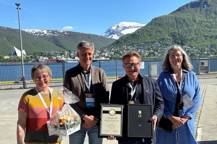 Fire personer som står ute med fjell i bakgrunnen